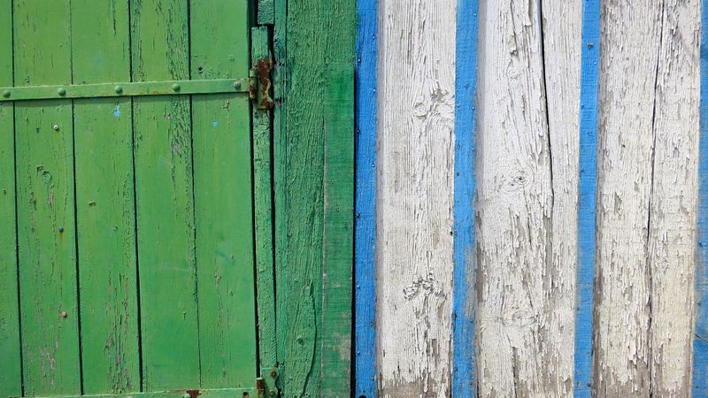 A photo of a green wooden door in a blue and white striped farm wall in northern France