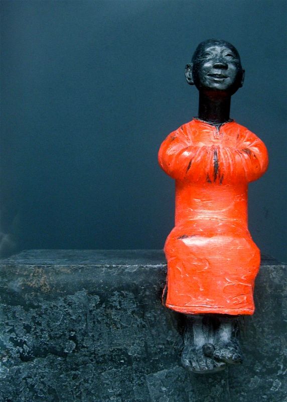 A photo of a small sculpture of a happy Buddhist monk sat on a ledge