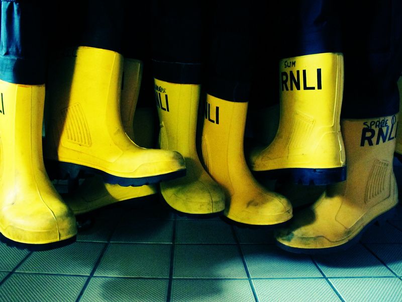 A photo of 8 yellow lifeguards wellies hanging from waterproof trousers in the RNLI shop in Weymouth
