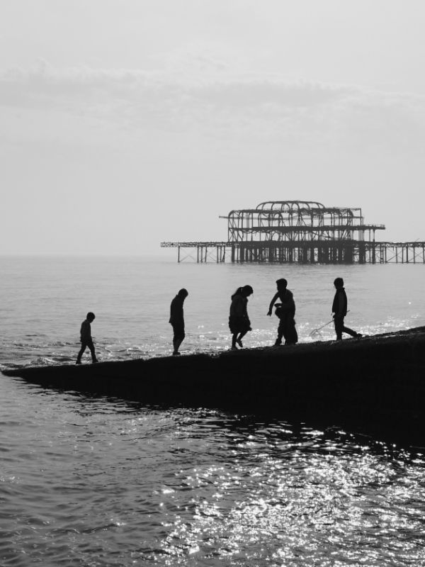 A black and white photo of some figures silhouetted against the ruins of the old Brighton pier