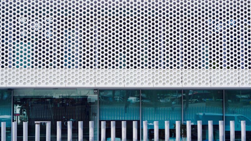 A photo of the side of an office building in Berlin. It has glass windows along the bottom and a white, metal, perforated sheet across the top