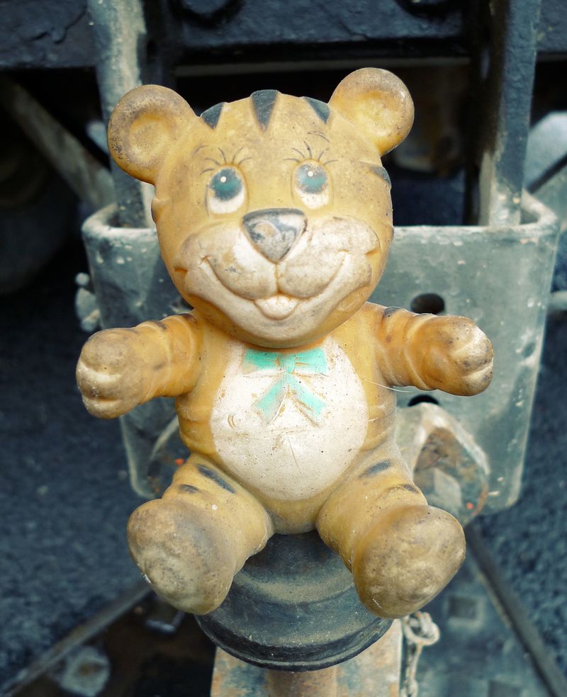 A photo of a grubby plastic tiger toy, stuck onto the tow-bar of a van