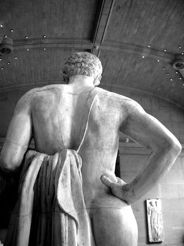 A black and white photo of the back of a marble statue of a man with a magnificent arse