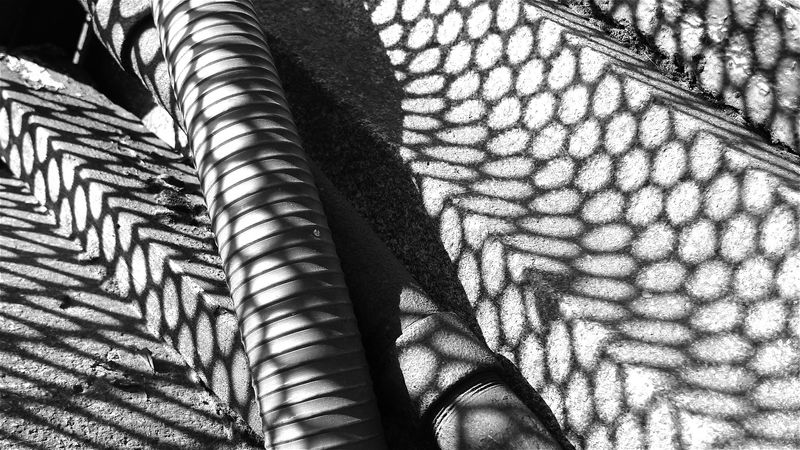 A black and white photo of some concrete and pipes with a honeycomb shadow over them
