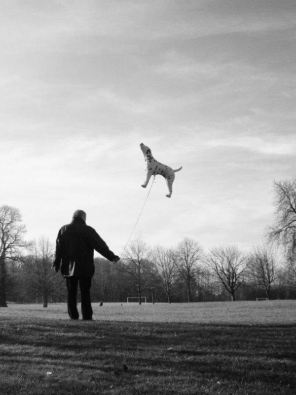 A black and white photo of my dad in the park holding a helium balloon on a string. The balloon is in the shape of a dog